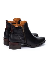 Botas de tobillo de cuero negro con un panel texturizado y acentos marrones. Cuentan con una cremallera lateral y un tacón bajo tipo bloque. El interior es de color naranja.