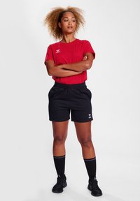 Röd bomullströja med en logotyp, svarta shorts med elastiskt midjeband, svarta knähöga strumpor och svarta idrottsskor. Enkla, avslappnade sportkläder.