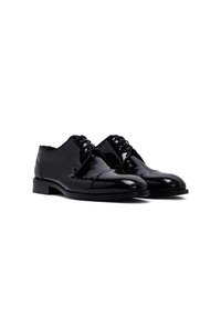 Souliers oxford en cuir noir poli avec des lacets fermés et un léger talon, présentés côte à côte sur un fond blanc.