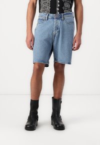 Shorts din denim de culoare albastru deschis, cu o croială relaxată, margine desfăcută și un design standard cu cinci buzunare, asortați cu botine din piele neagră până la gleznă.