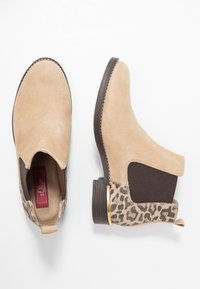 Stivali alla caviglia in suede beige con dettagli in stampa leopardata, pannelli laterali elasticizzati e tacco basso marrone. Dettagli in metallo dorato vicino al tacco.