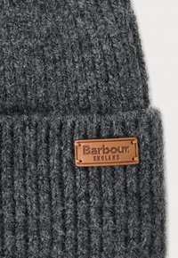 Szürke kötött sapka vastag, texturált gyapjú keverékből. Jellemzője egy barna bőr öntvény "Barbour" és "ENGLAND" felirattal.