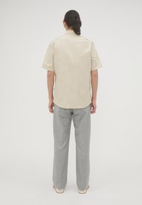 Korte mouwen beige shirt met een afgeronde zoom, gecombineerd met lichtgrijze broek. Glad materiaal met een ontspannen pasvorm, met subtiele stiksels.