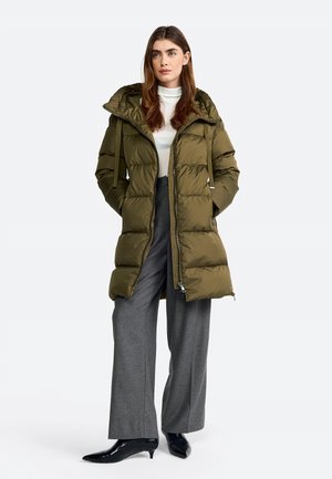 Manteau matelassé vert olive avec capuche, doté d'une fermeture éclair à l'avant, de poches latérales et d'un design matelassé texturé. Associé à un pantalon gris à jambes larges et des bottes noires.