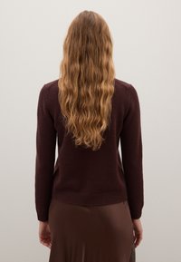 Bordeauxfarbener Wollpullover mit langen Ärmeln und geripptem Saum, von hinten betrachtet. Strukturiert Oberfläche, figurbetontes Design.
