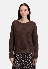 Bruine gebreide trui met een textuurpatroon, ronde halslijn en lange mouwen. Draagt bij een gemusterde rok met een luipaardprint.