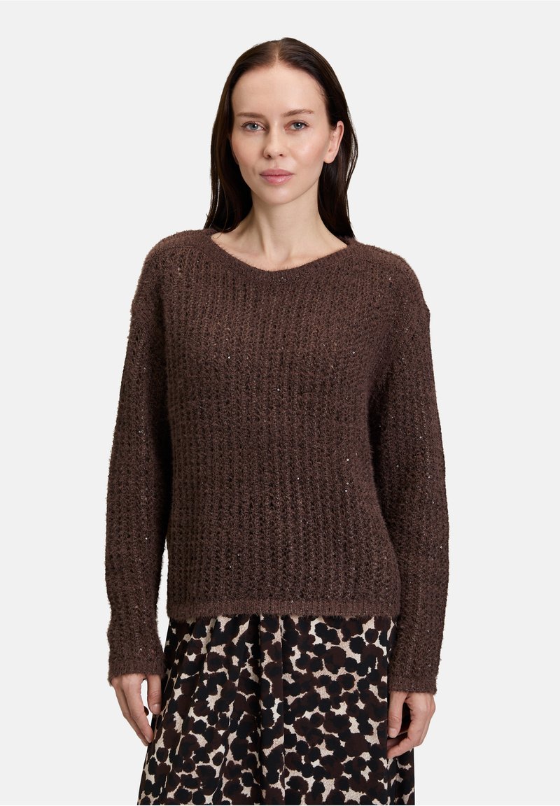 Bruine gebreide trui met een textuurpatroon, ronde halslijn en lange mouwen. Draagt bij een gemusterde rok met een luipaardprint.