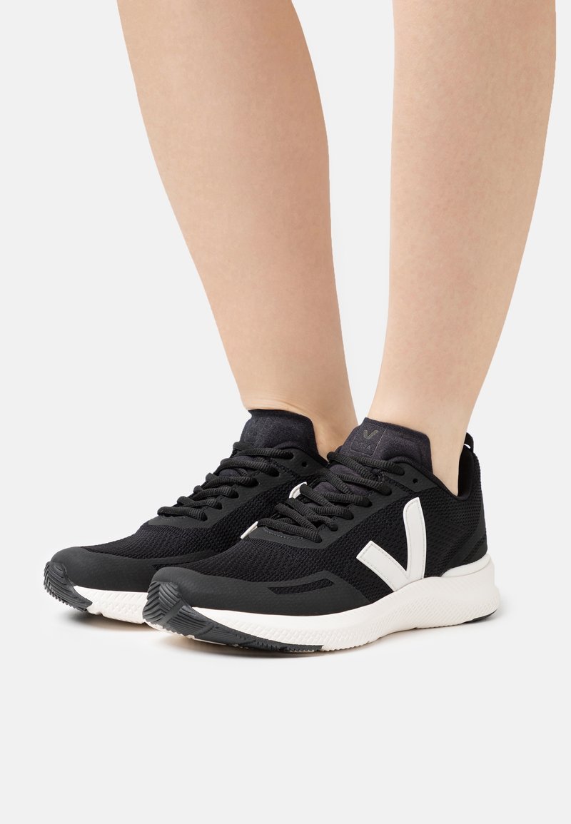 Black athletic shoes with a breathable mesh upper, white logo, and textured rubber soles for traction. Minimalist design with lace closure.