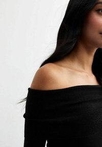 Schwarzes, geripptes Off-Shoulder-Top mit einem enganliegenden Schnitt um die Arme und einer strukturierten Oberfläche, die den Schulterbereich betont.