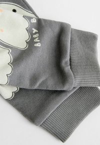 Vêtement en coton gris avec des poignets côtelés, affichant un graphique d'animal de couleur claire et le texte "BABY B." Texture douce avec un design décontracté.