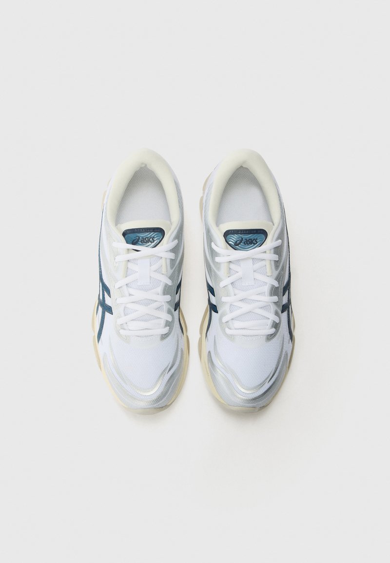 Baskets de sport blanches avec tige en maille, accents bleu marine et semelle texturée. Dotées de lacets blancs et d'une étiquette de langue de marque.