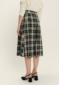 Černobílá kostkovaná sukně s sklady, do délky ke kolenům, vyrobená z tkané látky. Hladký povrch s přiléhavým pasem a rozšířeným siluetou.