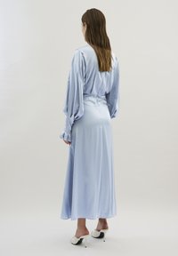 Rochie din satin de culoare albastru deschis, cu mâneci lungi și voluminoase și manșete franjurate, strânsă în talie, lungă până la glezne. Muli albe cu toc.