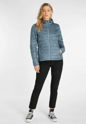Hellesblau, isolierte Pufferjacke mit Reißverschluss vorne, Kapuze, seitlichen Taschen und gestepptem Struktur. Kombiniert mit schwarzen Hosen und Turnschuhen.