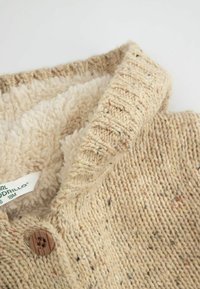 Beżowy sweter dzianinowy z kolorowymi akcentami. Posiada miękką, kremową podszewkę z polaru oraz detal w postaci guzika z przodu.