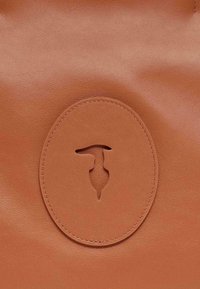 Borsa in pelle marrone con logo circolare in rilievo e design ritagliato al centro. Texture liscia con finitura opaca.