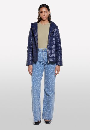 Giacca piumino blu navy scuro con finitura lucida, dotata di cappuccio e zip frontale. Abbinata a jeans a gamba larga con motivo blu chiaro.