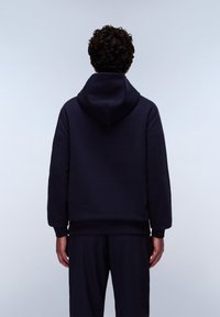Hanorac bleumarin cu glugă mare, cu manșete și tiv ribate; pare moale și căptușit cu fleece, purtat cu pantaloni bleumarin asortați.