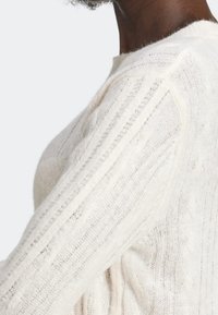 Suéter blanco de punto con un patrón texturizado y rayas verticales, con acentos de canalé en el cuerpo y las mangas. Material suave y ligero.