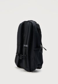 Μαύρο σακίδιο Columbia, εμφανιζόμενο από πίσω, με επενδυμένους ιμάντες ώμου, πλαϊνή τσέπη και ρυθμιζόμενο κλείστρο στο στήθος, σε λευκό φόντο.