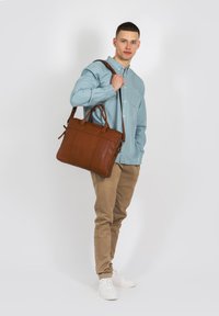 Geantă tote din piele maro, cu două mânere și o curea de umăr detasabilă, prezentând accente cusute și o finisare netedă, texturată.