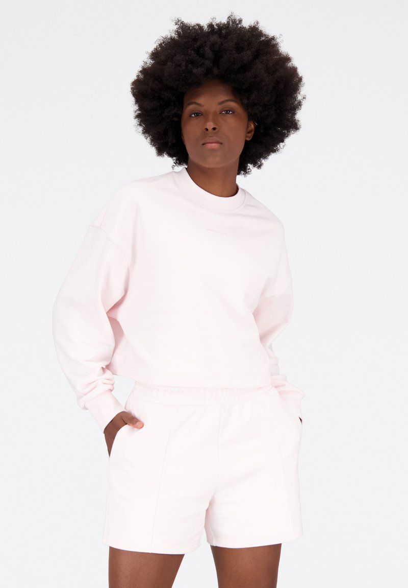 Sudadera rosa claro con cuello redondo y hombros caídos, combinada con pantalones cortos rosa claro a juego con una cintura elástica.