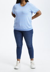 Lysblå kortærmet stribet sweater med hvide linjer, parret med mørkeblå skinny jeans og hvide sneakers. Glat strikket tekstur.