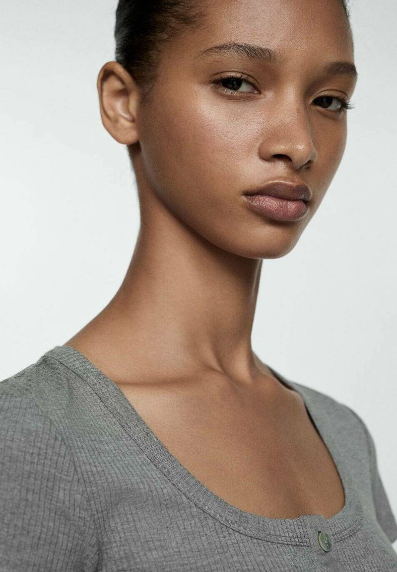 Top grigio a coste con scollatura a barca e piccolo dettaglio di bottoni. Tessuto morbido, design aderente che mette in evidenza la clavicola e l'area delle spalle.