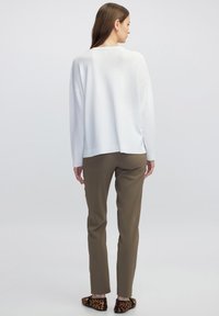 Witte, losvallende trui met verlaagde schouders; gecombineerd met olijfgroene broek; zwart en bruin luipaardprint flats aan de voeten.