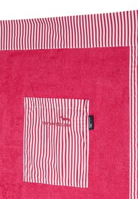 Toalla de color rosa brillante con superficie texturizada, con un bolsillo a rayas y un borde en blanco y rojo. Logo bordado en el bolsillo.