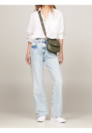 Sac bandoulière en cuir vert à silhouette incurvée, ferrures argentées et sangle ajustable ; porté avec une chemise blanche et un jean bleu clair.