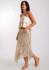 Top corto en capas beige con detalles metálicos, combinado con una falda brillante y estampada que presenta acentos de cuentas y una silueta fluida.