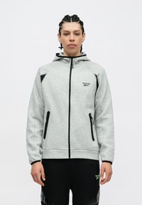 Šviesiai pilka zip-up gobtuvinė striukė su juodais akcentais, dviem priekinėms kišenėms ir raištelio gobtuvu. Papuošta Reebok logotipu ant krūtinės.
