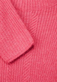 Rosa stickad tröja med ribbad textur och vikkrage. Mönstret visar en jämn, lätt fluffig väv.