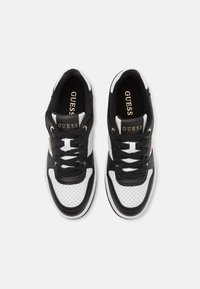 Schwarz-weiße Sneaker mit perforierter Vorderseite, goldenen Akzenten und schwarzen Schnürsenkeln. Sie haben ein Logo auf der Zunge und einen gepolsterten Kragen für zusätzlichen Komfort.