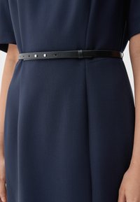 Marine jurk met een gladde textuur, voorzien van een zwarte leren riem met zilveren hardware en meerdere gaten voor aanpassing.