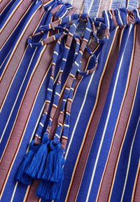Tessuto a righe blu e marrone con chiusura a cravatta e nappine blu. La texture è liscia con linee orizzontali di larghezze variabili.