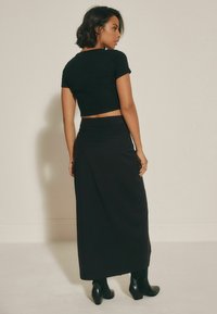 Top scurt negru cu mâneci scurte, combinat cu o fustă lungă neagră, cu talie ajustată și design minimalist. Botine negre cu toc.