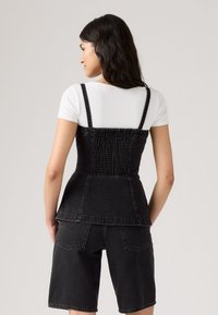 Črn jeans korzet s nabranim hrbtom, nastavljivimi naramnicami in oprijetim silhueto, v kombinaciji s temno jeans kratkimi hlačami.