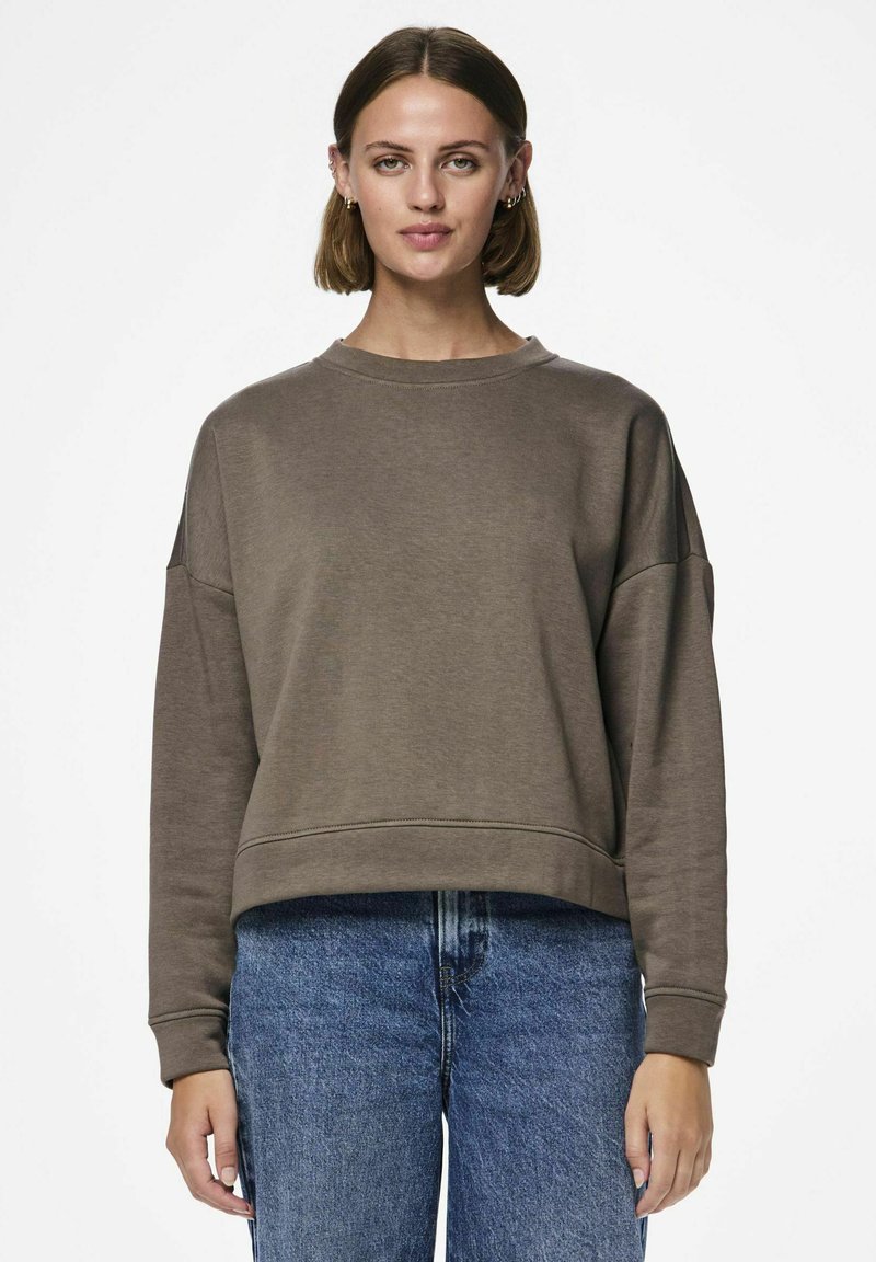 Felpa corta marrone con scollatura rotonda e spalle basse, realizzata in materiale morbido, abbinata a jeans blu a vita alta.
