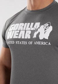 Siva atletska majica s velikim belim natpisom "GORILLA WEAR" i "UNITED STATES OF AMERICA" ispod, uz grafiku gorile.