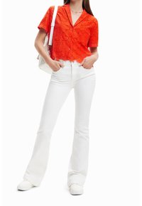 Blusa rossa a maniche corte con ricami floreali, abbinata a jeans bianchi a zampa d'elefante e scarpe slip-on bianche. Presenta un collo a V e un orlo ondulato.