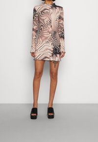 Une robe à manches longues présentant un motif ondulé rose et noir, le tissu a une texture lisse, avec un ourlet volanté et un col montant.