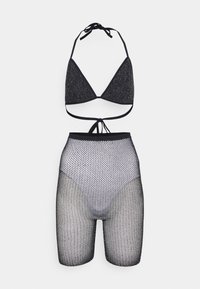 Top de bikini preto com copas triangulares, em tecido texturizado e brilhante, combinado com calções altos de rede preta com grandes buracos.