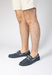 Marineblaue Lederbootsschuhe mit weißen Schnürsenkeln und Gummisohlen, die ein gestepptes Design und offene Seiten für Atmungsaktivität aufweisen.