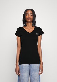 Zwarte v-hals t-shirt van zachte katoen, met korte mouwen en een klein logo op de linkerborst. Slanke pasvorm met een gladde textuur.