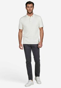 Weißes kurzärmliges Poloshirt mit vertikaler Ripp-Textur, mit einem Drei-Knopf-Verschluss, kombiniert mit dunkelgrauen Slim-Fit-Hosen und weißen Sneakers.