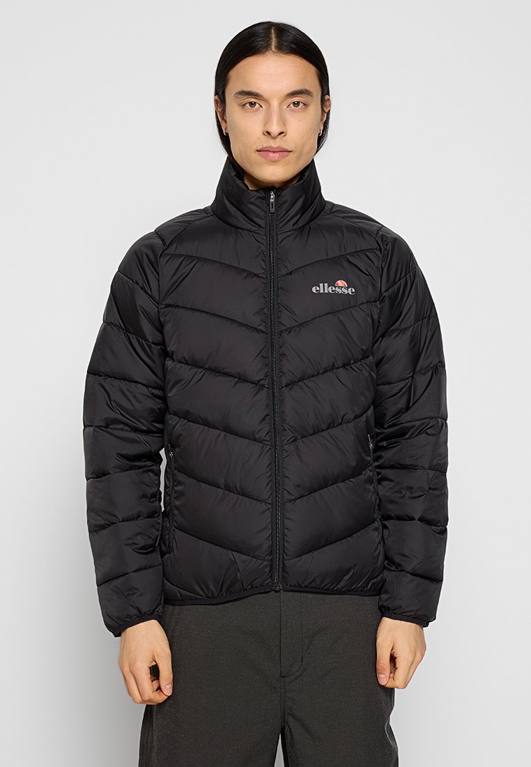 Giacca a vento nera con cuciture a zigzag, colletto alto, zip frontale completa e logo ricamato sul petto. Materiale morbido e isolato.