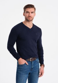 Marinblå v-ringad tröja i mjukt tyg, figursydd design med långa ärmar, matchad med blå jeans och brunt läderbälte.