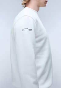 Felpa bianca in cotone con colletto a girocollo, maniche lunghe e logo ricamato sul braccio sinistro, che riporta "Napapijri Geographic SINCE 1987."